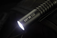 SPERAS EST SE 1500lm compact tactical EDC flashlight turned on resting on dark outdoor gear