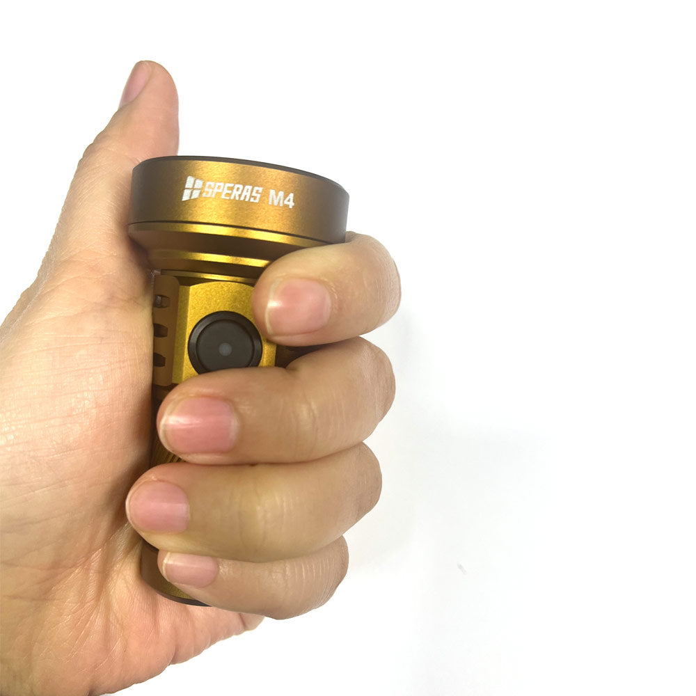 Hand holding the desert tan SPERAS M4 flashlight, demonstrating its ultra-compact, palm-sized dimensions for everyday carry