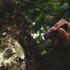 Rugged IP68 waterproof SPERAS EST SE tactical flashlight machined from 6061 aluminum alloy illuminating a tree trunk in the woods