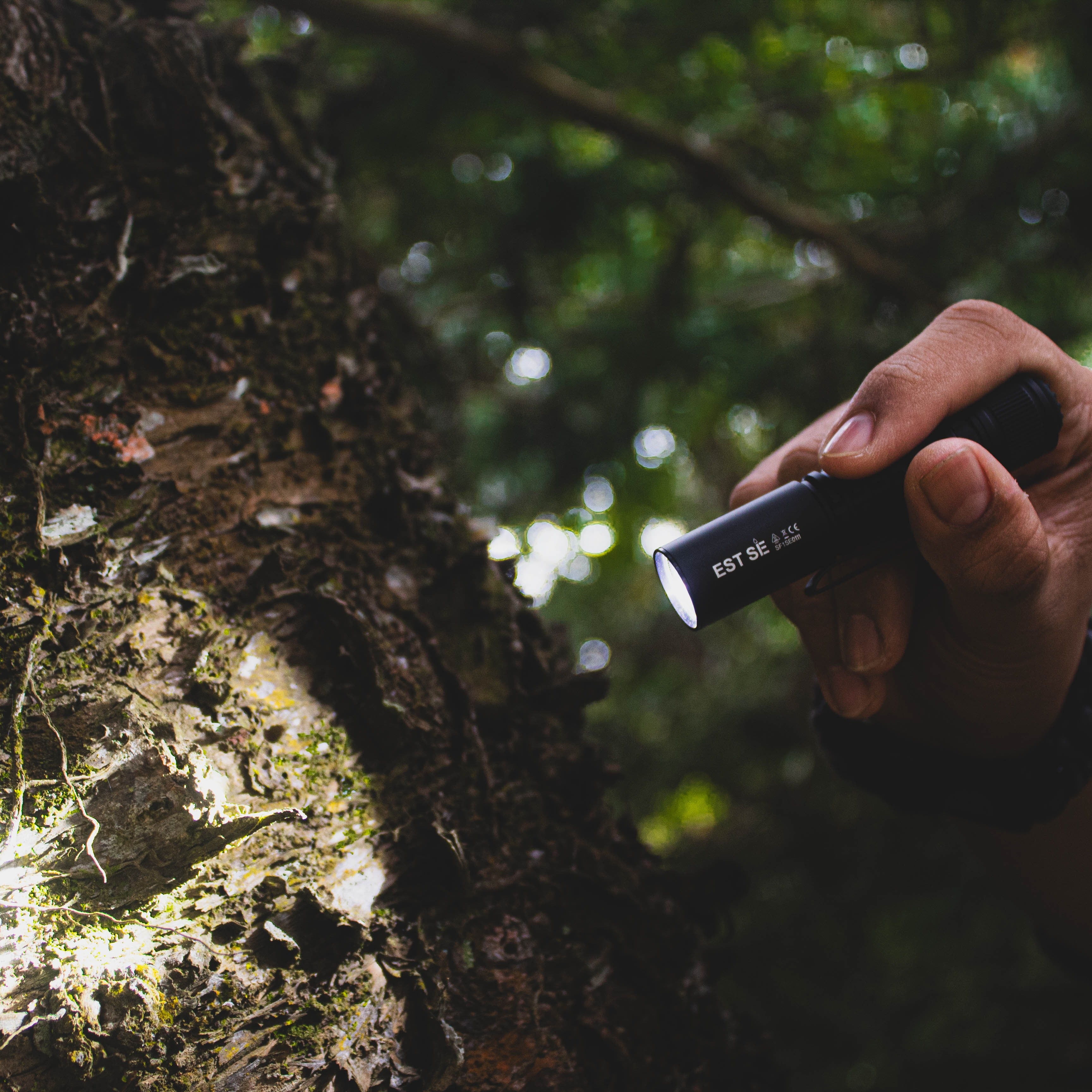 Rugged IP68 waterproof SPERAS EST SE tactical flashlight machined from 6061 aluminum alloy illuminating a tree trunk in the woods
